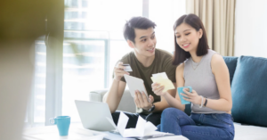 (Smiling couple reviewing bills and using a credit card at home, representing financial teamwork and stress-free debt management.)