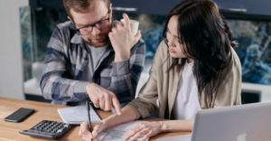 (A couple reviews financial documents at a kitchen table, using a calculator and laptop, highlighting collaboration in managing debt and budgeting.)