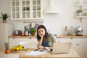 Frustrated upset young dark haired female feeling unhappy, reading notification from bank, sitting at kitchen table, doing paperwork and calculating budget. Fiannces, debts, accounts and mortgage